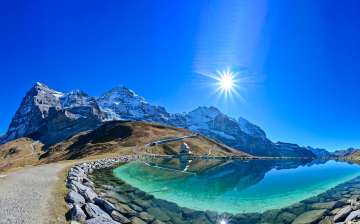 Der Fallbodensee bei der Kleinen Scheidegg liegt unter strahlendem Himmel. Im Hintergrund erheben sich Eiger, Mönch und Jungfrau .