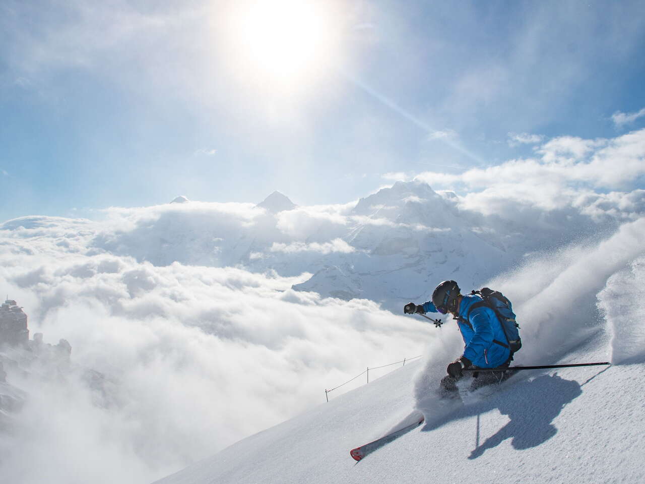 Telemark skier in action. The skier carves his turns in the snow in front of a magnificent panorama on the Schilthorn. The Eigern, Mönch and Jungfrau triumvirate looms out of the clouds in the background.