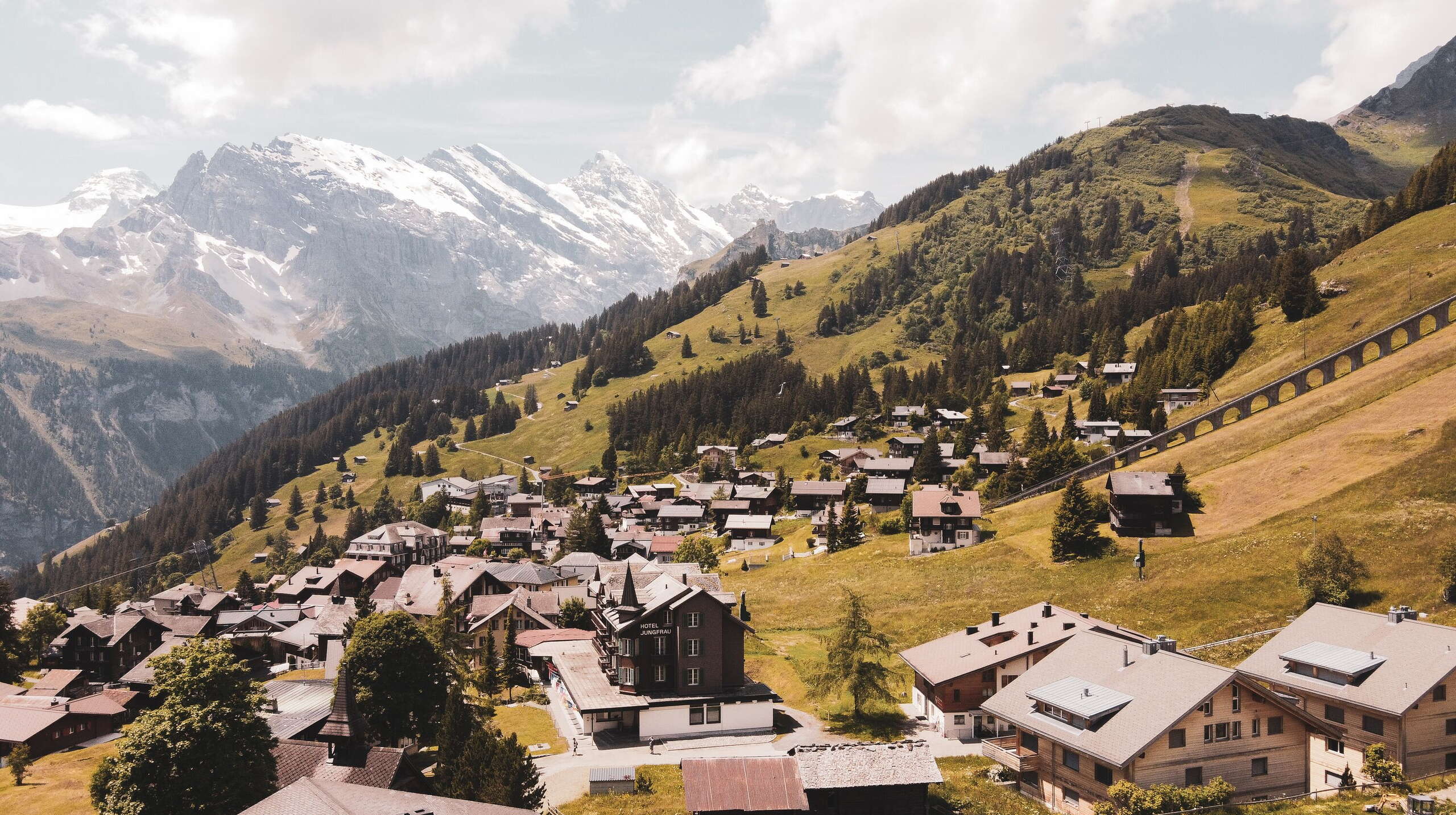 Herbstliche Luftaufnahme vom Dorf Mürren. Die Sonne scheint durch den leicht bewölkten Himmel.