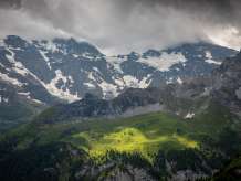 Aussicht von Schiltalp in die gegenüberliegende Seite des Tal, Richtung Tanzbödeli (links) und Busenalp erleuchtet im mystischem Licht. Im Hintergrund schneebedecktes Mittagshorn (links) und Breithorn (rechts) Berggipfel in Wolken eingedeckt.